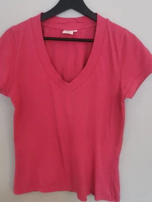 Rosa v-ringad t-shirt från Boomerang - En enkel och snygg rosa t-shirt med v-ringning och korta ärmar. T-shirten har en klassisk passform och är gjord i mjuk bomull som känns skön mot huden. Perfekt till jeans eller kjol för en avslappnad look. Är från Boomerang, storlek M. Är i fint använt skick. 