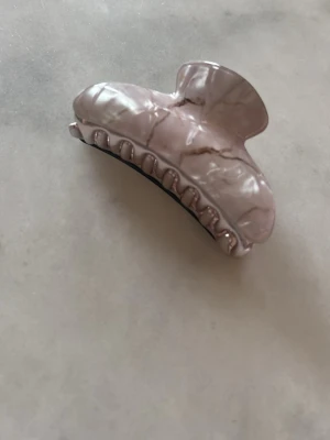 Ljusrosa hårklämma i marmormönster - Snygg hårklämma i ljusrosa med marmorerat mönster. Klämman har en klassisk form och är tillverkad i plast med metallfjäder. Perfekt för att snabbt sätta upp håret och ger en trendig touch till din look.