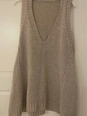 Beige stickad väst med v-ringning - Mysig beige stickad väst med djup v-ringning och bred ribbad kant nedtill. Västen har en loose passform och är perfekt att slänga över en skjorta eller t-shirt för en avslappnad look.