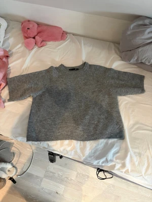Grå stickad tröja med korta armar  - Mysig grå stickad tröja med rund hals och avslappnad passform. Tröjan har halvlånga ärmar och är från lager 157 i Xs. 