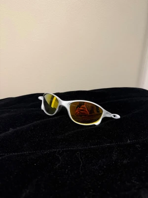 Oakley silvriga sportiga solglasögon - Säljer ett par riktigt sportiga solglasögon från Oakley med silvrig båge och spegelgula linser. De har en smal, futuristisk form och är tillverkade i lätt syntetmaterial. Perfekta för dig som vill sticka ut med en cool och modern look.