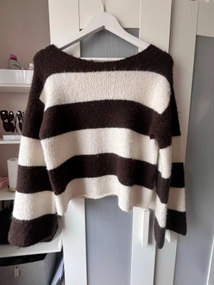 Randig stickad tröja Gina Tricot - Mysig stickad tröja från Gina Tricot med breda bruna och vita ränder. Tröjan har en avslappnad passform, långa ärmar och en något kortare, boxig modell. Perfekt för dig som gillar en trendig och bekväm stil.