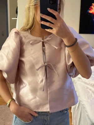 Ljusrosa puffärmsblus med rosetter - Supersöt ljusrosa blus med puffiga korta ärmar och två dekorativa rosetter framtill💞