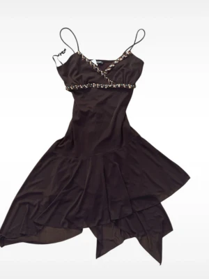 Brun asymmetrisk klänning sopranos - Brun kortklän dy med asymmetrisk nederkant från Sopranos. Klänningen har tunna axelband, omlott upptill och är dekorerad med pärlor i brunt, turkost och silver längs urringningen och under bysten. Tillverkad i ett mjukt, glansigt syntetmaterial.