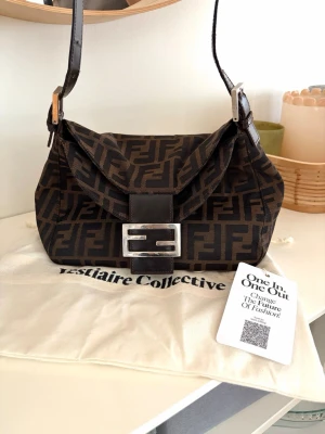 Fendi Baguette brun monogramväska - Säljer denna ikoniska Fendi Baguette väskan i brunt tyg med klassiskt FF-monogram. Väskan har ett justerbart axelband i läder och en silverfärgad spänndetalj framtill. Köpt på Vestiaire collective och är äkthetskontrollerad i deras varuhus i Paris.  Skickar såklart det elektroniska kvittot vid köp❤️