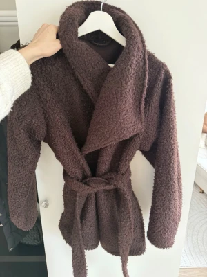 Brun teddyjacka från Gina Tricot - Mysig brun oversized teddyjacka från Gina Tricot med oversized krage och knytskärp i midjan. Jackan har lång ärm och är gjord i fluffigt teddy-material som ger en trendig look. Perfekt för dig som vill ha en varm och stylish jacka till hösten eller vintern.