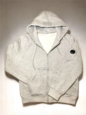Ljusgrå zip hoodie från C.P. Company - Ljusgrå hoodie med dragkedja från C.P. Company. Klassisk huva med dragsko, två fickor framtill och ribbade muddar. Ikonisk svart logodetalj på ärmen. Tillverkad i mjuk bomullsblandning för skön känsla.
