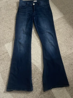 Mörkblå bootcut jeans - Mörkblå jeans med bootcut-modell och utsvängda ben. Klassisk femficksdesign och hög midja. Jeansen har subtila slitningar framtill och är perfekta att styla med sneakers eller boots. Materialet är mjukt och följsamt för en bekväm känsla.