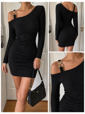 Svart ribbad oneshoulder klänning - Trendig svart ribbad kortklänning med oneshoulder-design och lång ärm. Klänningen har en snygg metallring-detalj på axelbandet och figurnära passform som framhäver siluetten. Perfekt för dig som vill ha en stilren och modern look. Testad en gång annars oanvänd, kan ha tvättat den med.
