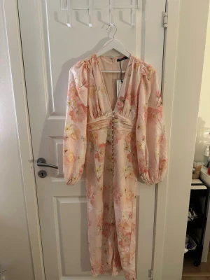 Rosa Blommig långklänning från Gina - Helt ny klänning från Gina tricot i storlek 36 som är slutsåld. Klänningen har djup v-ringning, puffiga långärmar och dekorativa knappar framtill. Perfekt klänning för sommaren☺️