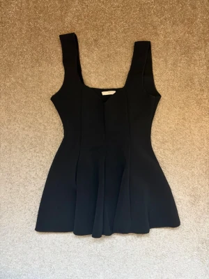 Svart topp från Zara - Stilren svart topp från Zara med breda axelband och figurnära passform upptill. Nertill har lätt utsvängd form som ger en snygg siluett. Perfekt för dig som gillar minimalistisk och modern stil. 