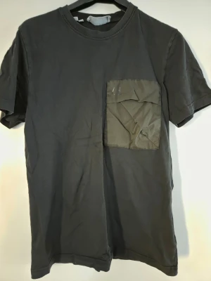 Svart t-shirt med ficka från Selected Homme - Cool svart t-shirt från Selected Homme med en kontrasterande ficka på bröstet. T-shirten har rund hals och korta ärmar, perfekt för en avslappnad look. Materialet är mjuk bomull och fickan har en lite glansig finish som sticker ut.