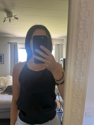 Svart linnetopp med spetsdetalj - svart linnetopp med tunna axelband och spetsdetalj i ryggen. Materialet känns lätt och luftigt.