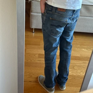Blå jeans från Nudie - Modell: Grim Tim. Storlek: W33 L34. Höger ficka fram har hål + lite slitet på höger knä men inget som syns - se bild 5