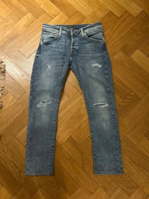 Jack & Jones Glenn jeans  - Säljer ett par blå jeans från Jack & Jones med slitningar på låren och knäna. Nyrpsig ligger på runt 699kr men här kan dom köpas för bara 149kr. Vid fler frågor är det bara att skriva!