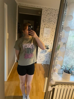 Grön loose-fit t-shirt med tryck - Säljer en grön t-shirt med loose passform och ett stort grafiskt tryck i vitt, svart och rosa på bröstet. T-shirten har korta ärmar och rund halsringning. Mindre lagning under trycket. 