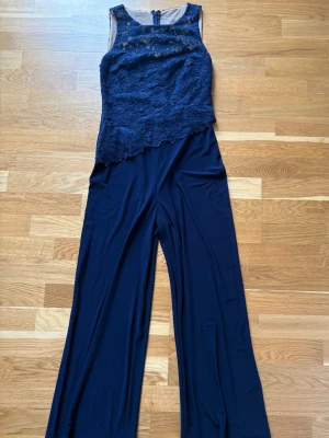 Mörkblå spetsjumpsuit med vida ben från Ralph Lauren - Supersnygg mörkblå jumpsuit med ärmlös överdel i spets och vida ben. Överdelen har vacker spetsdetalj och dragkedja bak. Perfekt för dig som vill sticka ut med en elegant och trendig look. Bara använd en gång! OBS! Den var för lång för mig så är uppsydd i benen (se bild) Jag är 159 cm och hade den med höga klackar. Det finns många cm över från hälarna. Hellängd från axelband 143 cm. Beninnerlängd 68 cm. Vida ben 20 cm. Mellan armhålorna 38 cm. RL strl 6. Nypris över 2000kr.