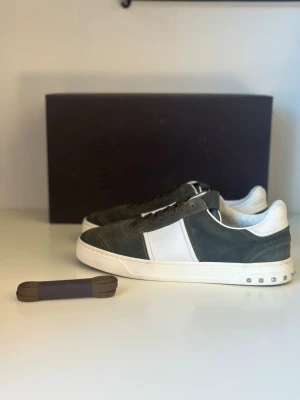 Gröna sneakers från Valentino - Stilrena sneakers från Valentino i grön mocka med vit läderdetalj på sidan och vit sula. Låga i modellen med dekorativa nitar på hälen och bruna skosnören. Perfekta för dig som gillar en clean och exklusiv look. Storlek 39 men passar mer 40-41