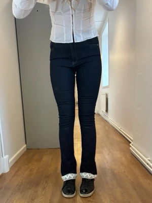 Mörkblåa flarejeans - Vi skulle säga att de här jeansen är mer flare än bootcut då de är lite smalare nertill🫶De har en snygg mörkblå färg, vit spets längst ner och är midwaist😊Måtten är: innerbenslängd - 86 cm,  midja - 80 cm och lårvidd - ca 46 cm. Storleken är en uppskattning så vi rekommenderar att ni mäter ovanstående mått på er själva!!💙