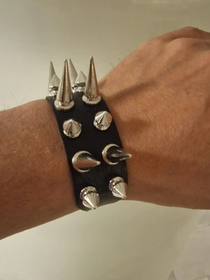 Armband punk med spikar - Armband punk med spikar. Europeisk och Amerikansk punkstil. 2-rads spikförsedd fauxläderarmband. Längd 25,8 cm. Bredd 2,6 cm.