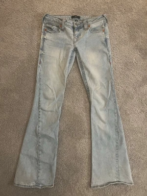 Ljusblå bootcut jeans True Religion - Säljer ett par ljusblå bootcut jeans från True Religion med klassiska kontrastsömmar och snygga detaljer på bakfickorna. Dessa jeans är väldigt sällan använda! Bara 2-3 gånger. Dom är i en perfekt ljus färg för våren och sommaren! PRIS KAN DISKUTERAS!