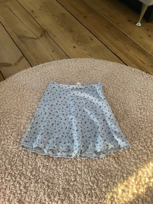 Ljusblå blommig kortkjol - Söt ljusblå kortkjol med små blommor i mörkare blått. Kjolen har en lätt utsvängd form och är gjord i ett tunt, mjukt material som känns perfekt för varmare dagar. Enkel att matcha med både toppar och sneakers.