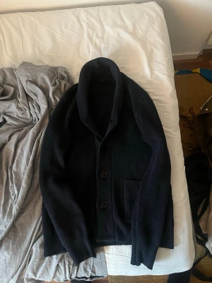 Mörkblå cardigan - Mörkblå cardigan med två stora knappar framtill och en bred krage. Koftan är tillverkad i ett tjockt, mysigt material som passar perfekt när det är kyligt ute. Långärmad och stilren design. Storlek L och knappt använd väldigt bra skick! Säljer för att jag den är för liten, hör av er vid frågor!