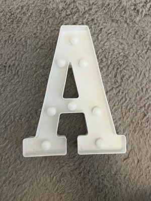 Vit LED-bokstav A i plast - Säljer en vit dekorativ LED-bokstav A i plast med små lampor som lyser upp bokstaven. Perfekt som personlig inredningsdetalj eller nattlampa. Batteridriven med plats för 2 AA-batterier och har en enkel av/på-knapp på baksidan.