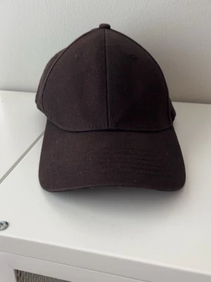 Enkel brun keps i bomull - Säljer en stilren svart keps med klassisk form och böjd skärm. Kepsen är tillverkad i bomull och har en neutral design utan logga eller mönster. Perfekt för dig som gillar en clean och avslappnad look.