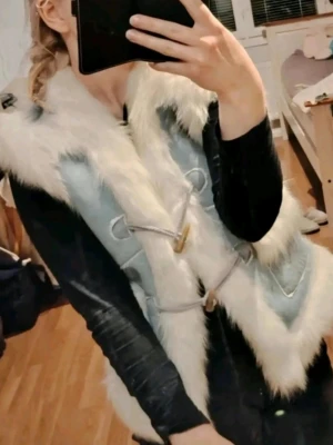 Vintage ljusblå pälsväst med vita detaljer☀️  - Snygg ljusblå pälsväst med fluffig vit fuskpäls längs kanterna och på fickorna💎 Västen har två dekorativa knäppningar framtill i trä och snöre. Perfekt för att ge din outfit en cool och trendig touch😍🩵 Vintage❤️ 