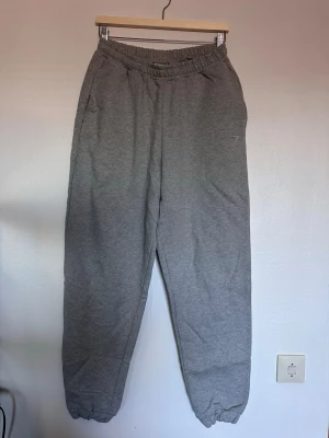 Grå mjukisbyxor från Gymshark - Säljer ett par grå baggie mjukisbyxor från Gymshark med resår i midjan och vid bensluten. Byxorna har sidofickor och en liten broderad logga på vänster lår. Perfekta för chill dagar eller träning.