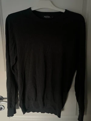 Mörkgrå stickad tröja Dressmann - Mörkgrå stickad tröja från Dressmann i mjuk supima-bomull. Klassisk rund halsringning och långa ärmar. Perfekt basplagg med enkel och stilren design som passar till det mesta.