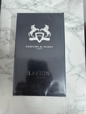 Parfums de Marly Layton EdP 125ml - Lyxig parfym från Parfums de Marly, modellen Layton. Flaskan kommer i en elegant mörkblå kartong med silverdetaljer och klassisk logga med två hästar. Eau de Parfum tillverkad i Frankrike, känd för sin exklusiva doft och stilrena design.