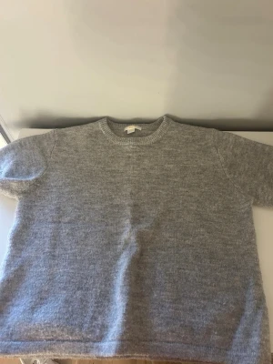 Ljusgrå stickad tröja - En enkel och stilren ljusgrå stickad tröja med rund halsringning och långa ärmar. Tröjan har en mjuk och fluffig känsla, perfekt för lager på lager. Passar till både jeans och kjol för en avslappnad look.