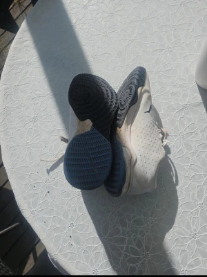 Vita Puma sneakers med blå detaljer - Säljer ett par vita Puma sneakers med blå detaljer och perforerade sidor för extra ventilation. Skorna har en låg profil och slitstark gummisula med mönster för bra grepp. Klassisk snörning och diskret Puma-logga på sidan.