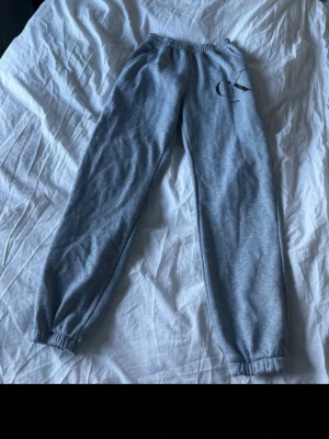 Grå mjukisbyxor  - Snygga grå mjukisbyxor från med elastisk midja och muddar vid bensluten. Byxorna har en enkel design med CK-logga på ena benet och är tillverkade i mjukt material som är skönt att ha på sig.