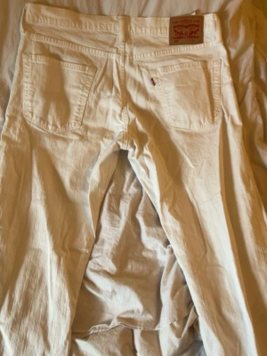 Vita Levi's jeans med rak passform - Säljer ett par vita jeans från Levi's med klassisk rak passform och fem fickor. Jeansen har Levi's ikoniska läderpatch bak i midjan och är tillverkade i bomull. Perfekta för en clean och stilren look.