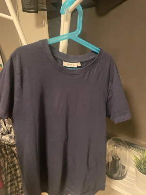 Mörkblå basic t-shirt från RYLS - En enkel och stilren mörkblå t-shirt från RYLS. T-shirten har rund halsringning och korta ärmar. Tillverkad i mjuk bomull som känns skön mot huden. Perfekt att matcha med jeans eller shorts för en clean look. Helt nytt skick, hör av er vid minsta fundering!