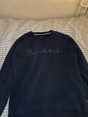 Mörkblå sweatshirt från Bondelid - Mörkblå sweatshirt från Bondelid med broderad logga på bröstet. Tröjan har rund halsringning och långa ärmar. Tillverkad i mjukt bomullsmaterial för en avslappnad och stilren look. Passar även S