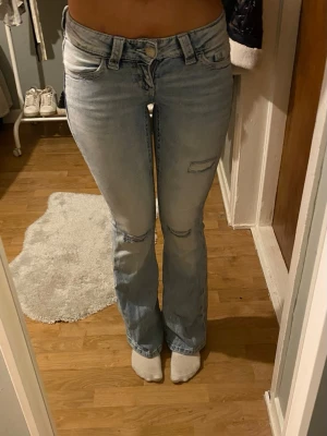 Ljusblå bootcut jeans med brodyr - Säljer ett par ljusblå bootcut jeans med slitningar framtill och snygg broderad detalj på bakfickan. Jeansen har normal midja och klassisk femficksmodell. 