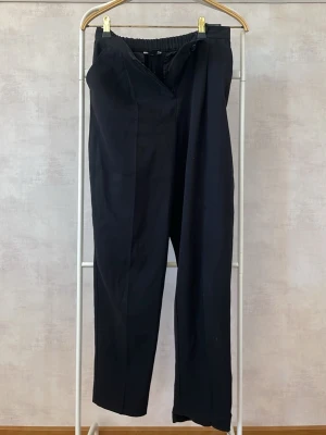 Svarta kostymbyxor med resårmidja - Snygga svarta kostymbyxor med rak passform och resår i midjan för extra komfort. Byxorna har pressveck framtill, två fickor bak och stängs med knapp och dragkedja. Perfekta för en stilren och avslappnad look.