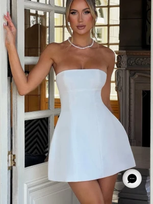 Vit axelbandslös kort klänning - Supersnygg vit axelbandslös kort klänning med figurnära passform och lätt utsvängd kjol. Klänningen har en enkel och stilren design som ger en elegant look. Perfekt för dig som vill sticka ut med en klassisk och fräsch outfit. I storlek S från baby boo