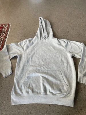 Ljusgrå hoodie från 157 i storlek L - Ljusgrå hoodie från 157 med klassisk känguruficka och huva. Mjuk insida och ribbade muddar vid ärmslut och nederkant. Perfekt för en chill och avslappnad stil. Materialet är en bomullsblandning som känns skön mot huden.