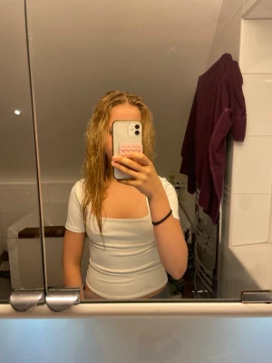 Vit topp med fyrkantig hals - Säljer en vit, tight topp med korta ärmar och snygg fyrkantig halsringning. Perfekt för dig som gillar en clean och stilren look. Materialet ser ut att vara stretchigt och bekvämt, passar till jeans eller kjol.