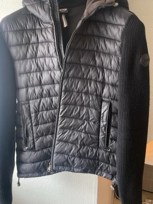 Svart pufferjacka från Colmar - Svart cardigan från colmar. Jackan har lite miss färgning i luvan men från de är den i väldigt bra skick, drag kedjor funkar som de ska. Passar perfekt för en som är 183/184, den är lite lite kort för mig på 189 cm men funkar verkligen endå.Man får med sig galge.