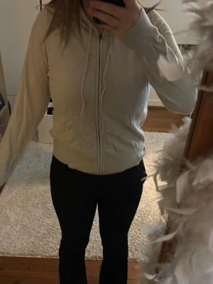 stickad Beige hoodie med dragkedja - Säljer en stickad  beige hoodie med dragkedja framtill och huva med dragsnören. Hoodien har ribbade muddar vid ärmslut och nederkant, samt en enkel och clean design utan synligt märke. Perfekt för en avslappnad och stilren look.