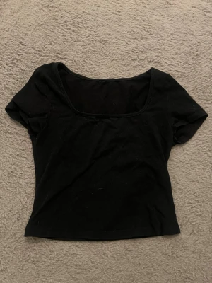 Svart croppad topp med kort ärm - En enkel svart croppad topp med korta ärmar och rundad urringning. Perfekt att matcha med jeans eller kjol för en clean look. Tunn och mjuk i materialet, passar till många olika stilar. Aningen tajt på mig dom brukar ha S