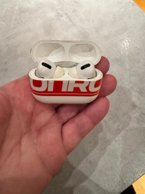 Apple AirPods Pro med ONROADERS-fodral - Säljer ett par Apple AirPods Pro med vitt och rött ONROADERS Podcast-samarbetsfodral. Trådlösa in-ear-hörlurar med silikonproppar och laddningsetui i plast. Snygg och unik design med tydlig logga på fodralet.