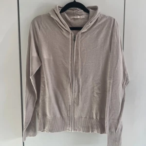 Beige hoodie med dragkedja - Ljusbeige cardigan från lager 157 med dragkedja framtill och huva. Tillverkad i ett tunt, mjukt material som känns skönt mot huden. Långa ärmar och ribbade muddar vid ärmslut och nederkant. Perfekt för en avslappnad och stilren look. Använd fåtal gånger. 