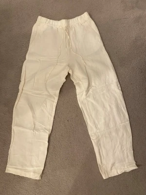 Vita linnebyxor - Säljer ett par vita linnebyxor med avslappnad passform och resår och knytning i midjan. Byxorna är raka i modellen och tillverkade i ett luftigt linnetyg.